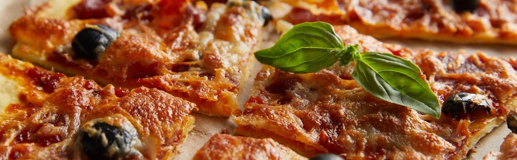 vista de cerca de la deliciosa pizza italiana con albahaca cortada en trozos en papel de hornear, plano panorámico
 - Foto, Imagen