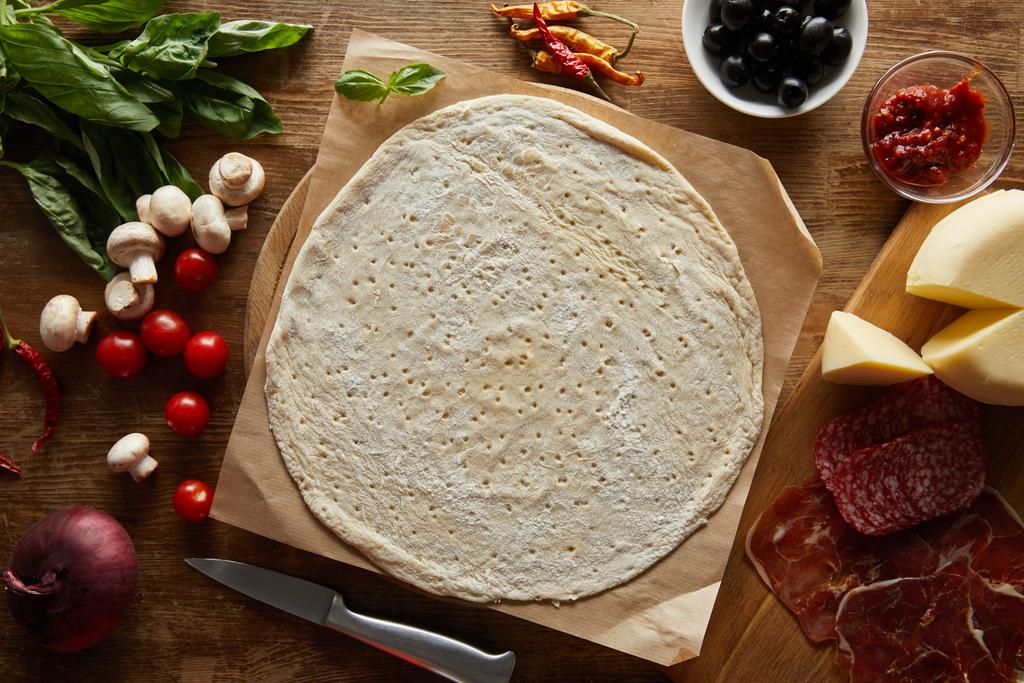 vista superior de masa cruda con ingredientes para pizza en mesa de madera
 - Foto, imagen