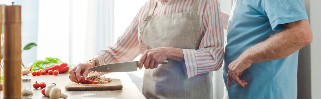Gewassen uitzicht van de man staan door vrouw snijden groenten op keukentafel, panoramisch schot  - Foto, afbeelding