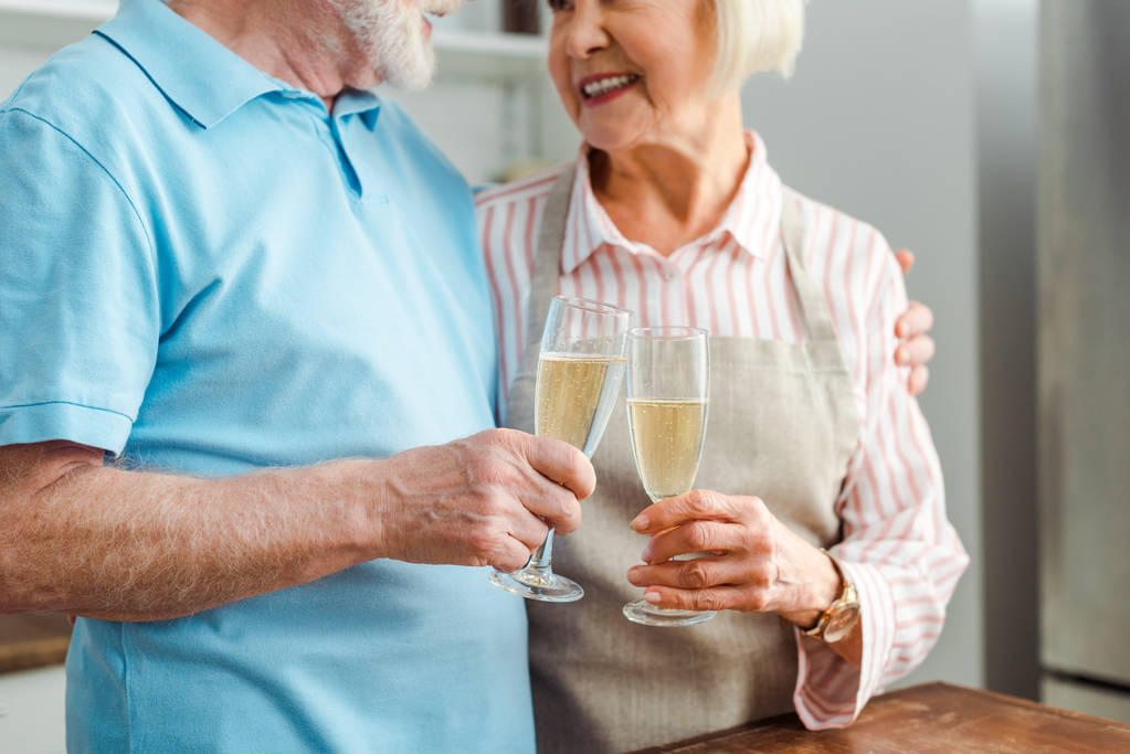 Rajatut näkymät vanhempi pari hymyilee toisilleen samalla clincing samppanjaa keittiössä
 - Valokuva, kuva