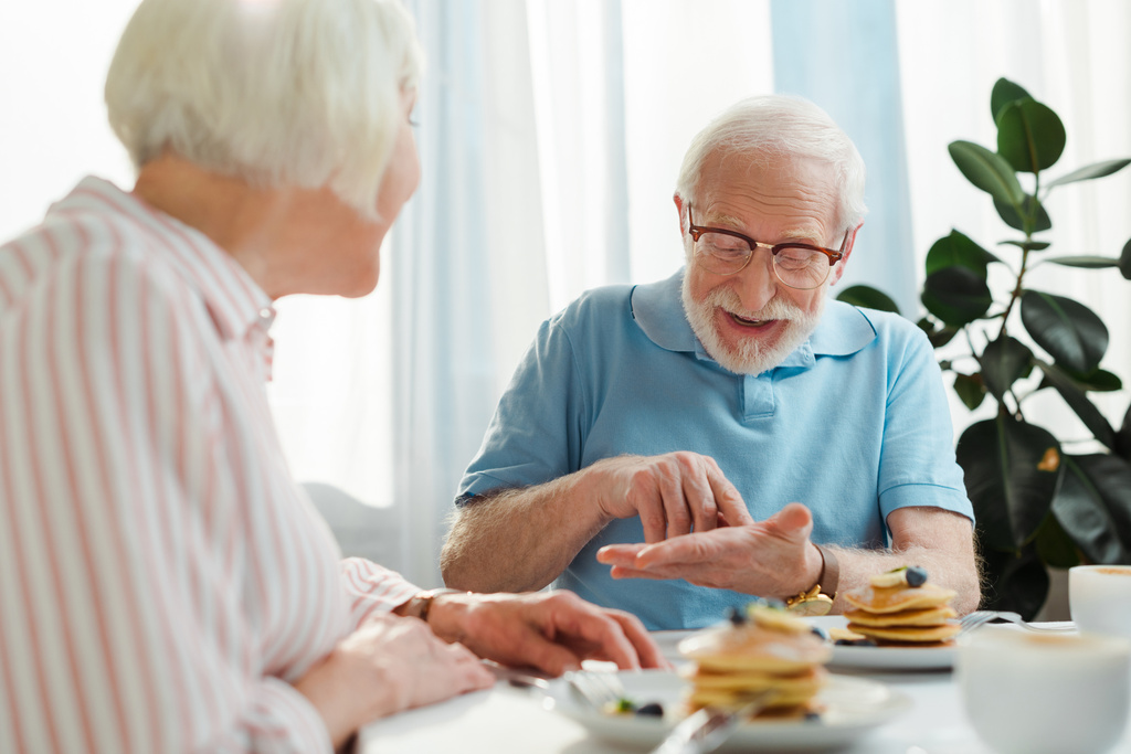 Enfoque selectivo del hombre mayor hablando con la esposa por café y panqueques en la mesa
  - Foto, Imagen