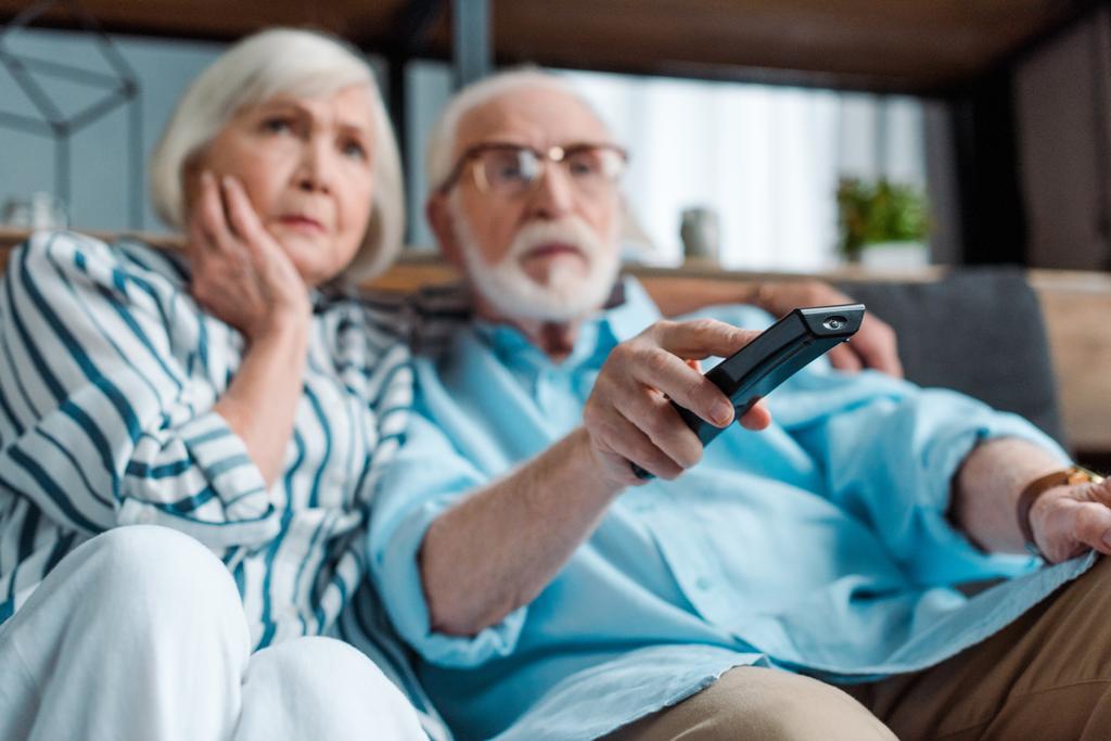 Selective focus of focused senior couple watching tv on couch in living room - Photo, Image