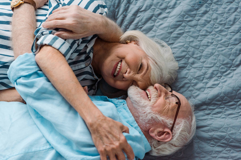 Widok z góry pary seniorów uśmiechających się i przytulających na łóżku - Zdjęcie, obraz