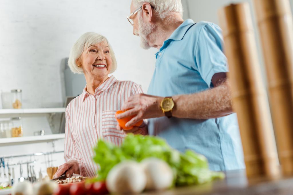 Вибірковий фокус усміхненої жінки, дивлячись на чоловіка під час приготування їжі на кухонному столі
 - Фото, зображення