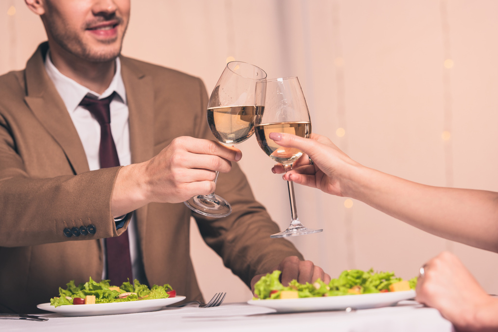 vista ritagliata dell'uomo che si stringe i bicchieri di vino bianco con la ragazza mentre si siede nel ristorante
 - Foto, immagini