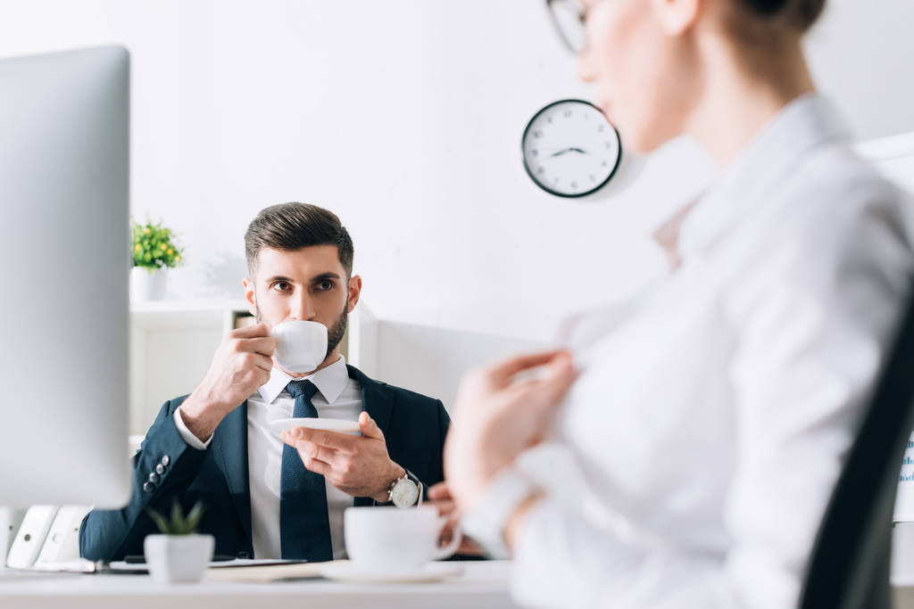 selektiver Fokus des Geschäftsmannes, der Kaffee trinkt und Sekretärin im Büro betrachtet  - Foto, Bild