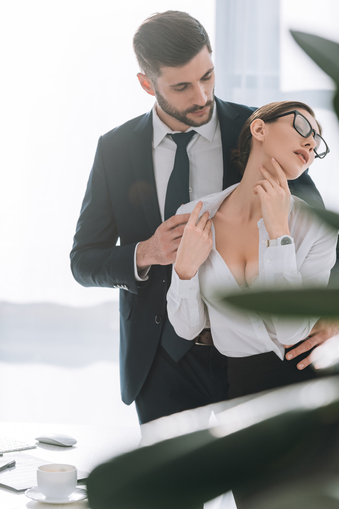selectieve focus van zakenman knuffelen sexy secretaresse met grote borst in kantoor  - Foto, afbeelding