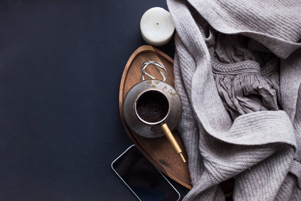 Winter cozy concept. Flatlay of gray knitted sweater, candle, coffee drink, diary, phone, glasses on black  table. Warm weekend in cold weather. dark atmosphere - Photo, Image