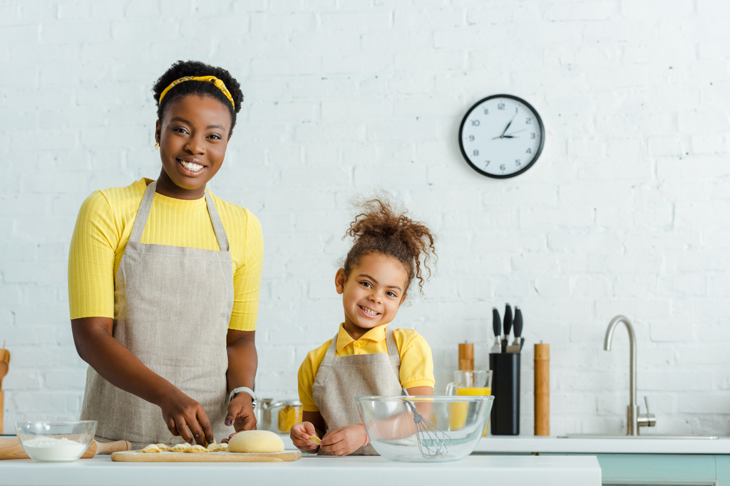 Χαρούμενη Αφροαμερικανή μητέρα και χαριτωμένη κόρη που σμιλεύει ζυμαρικά στην κουζίνα  - Φωτογραφία, εικόνα