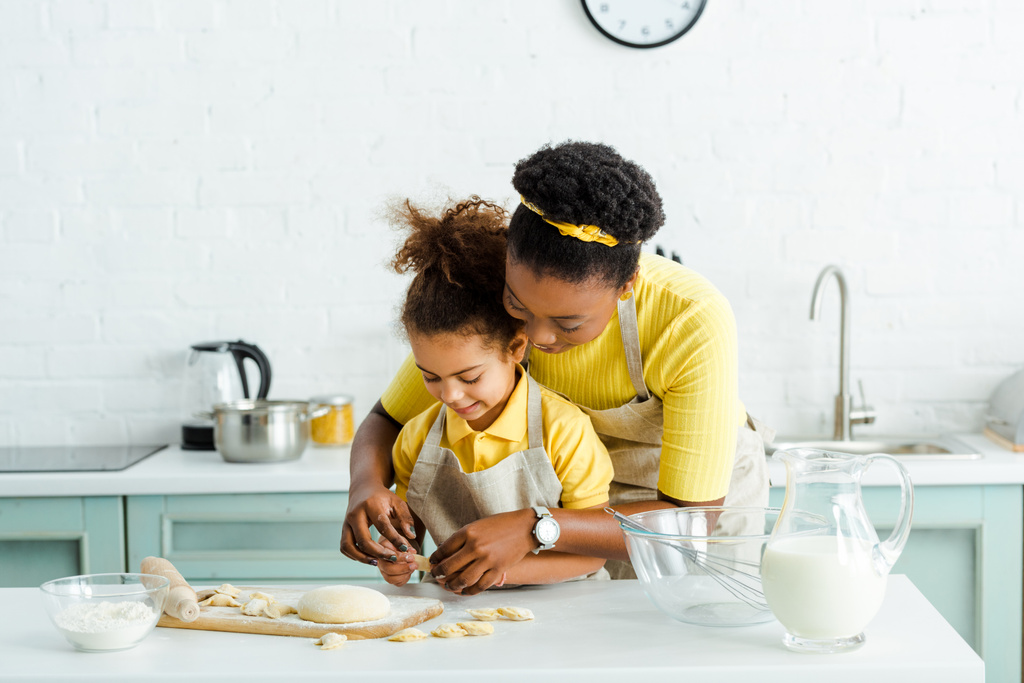 happy african american mother near cute daughter sculpting dumplings in kitchen  - Photo, Image