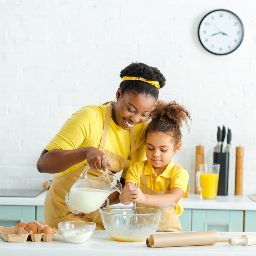 cheerful african american mother pouring milk in bowl near adorable kid  - 写真・画像