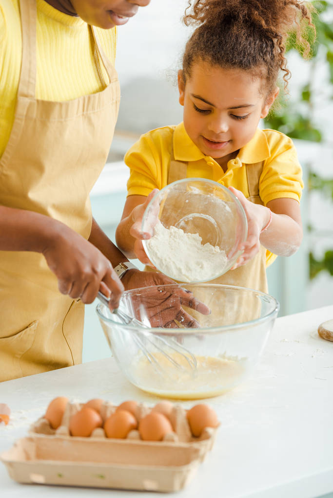 вибірковий фокус милої афроамериканської дитини, що тримає миску з борошном біля матері на кухні
  - Фото, зображення