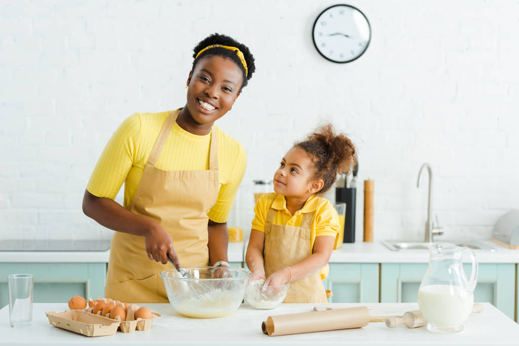 słodkie Afryki amerykański dzieciak patrząc na szczęśliwy matka a wprowadzenie ręce w misce z mąki  - Zdjęcie, obraz