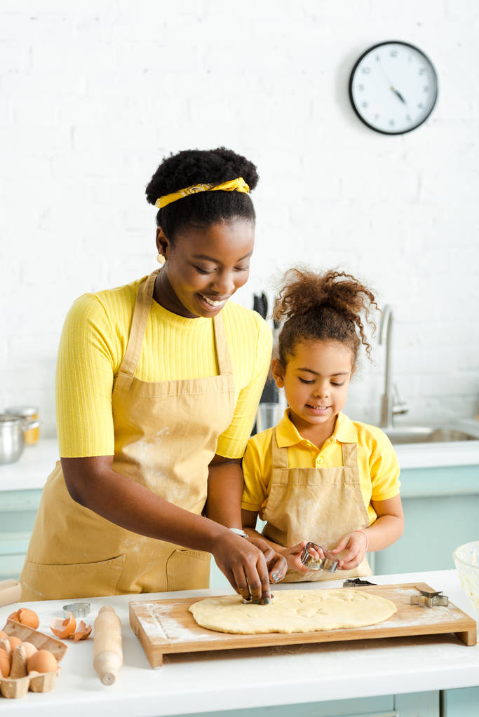niño afroamericano y feliz madre sosteniendo cortadores de galletas cerca de masa cruda
  - Foto, imagen