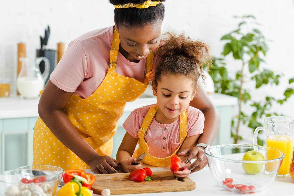 heureux afro-américain enfant coupe poivron près de la mère dans la cuisine
  - Photo, image