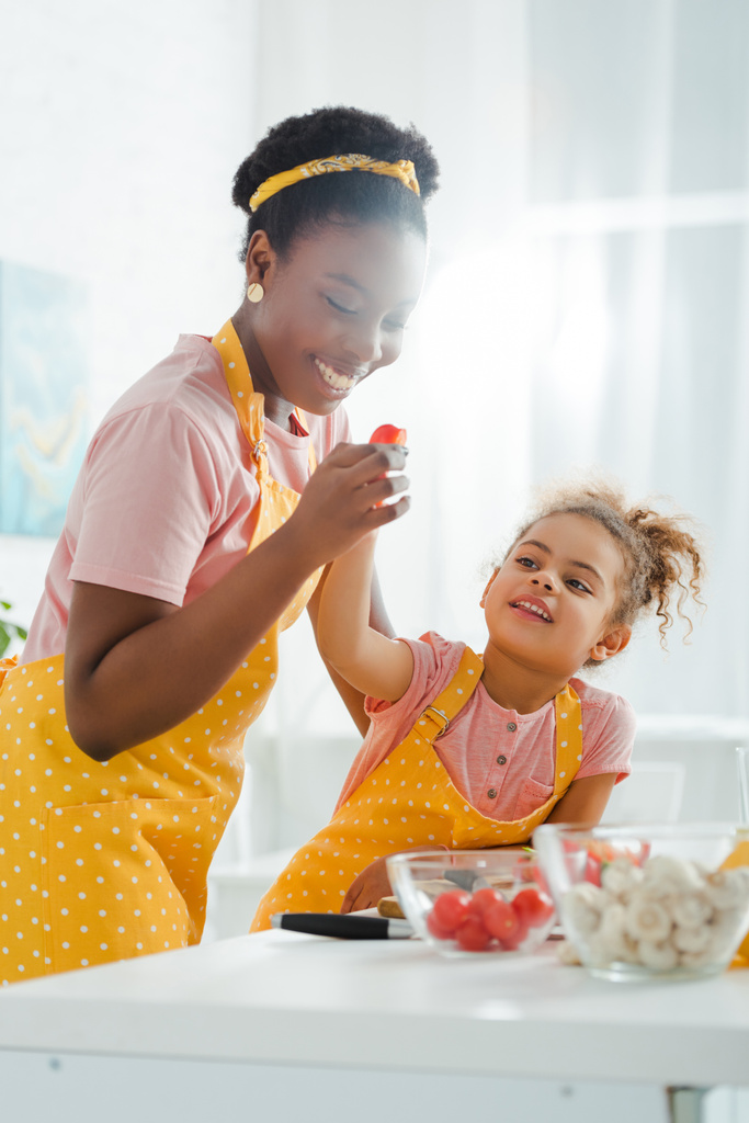 selective focus of happy african american mother holding cherry tomato near kid  - Photo, Image