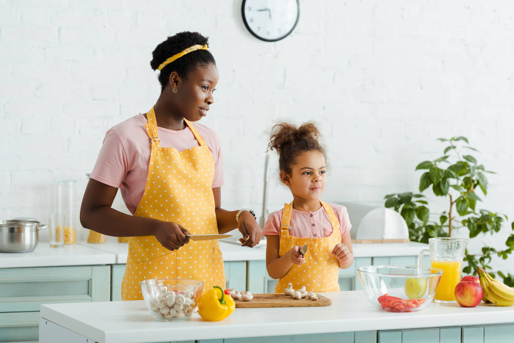 african american mother and daughter holding knifes near vegetables and fruits  - Photo, Image