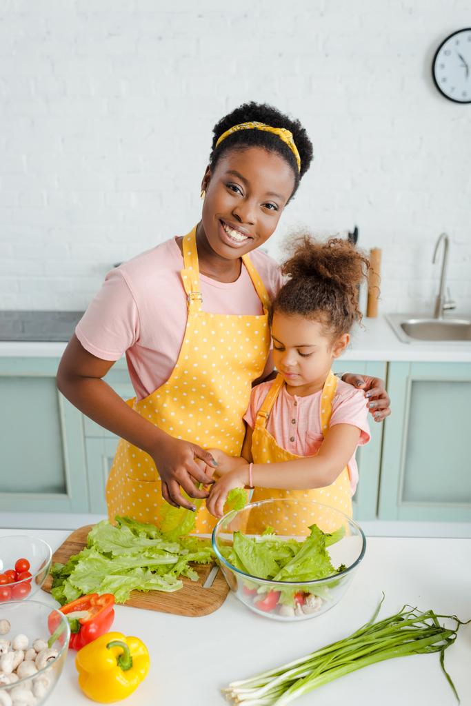 vidám afro-amerikai anya és aranyos gyermek készül saláta  - Fotó, kép