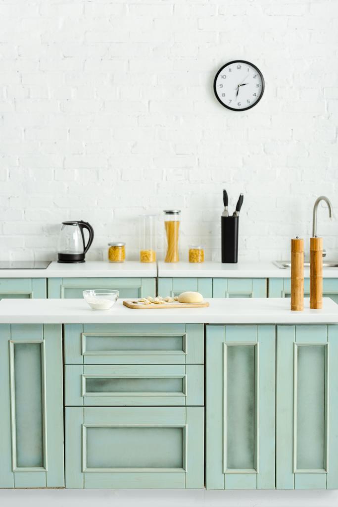 bolinhos crus na placa de corte de madeira perto da tigela com farinha na cozinha
  - Foto, Imagem