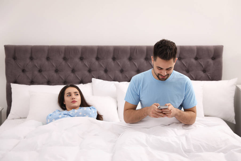 Młody mężczyzna woli smartfona od swojej dziewczyny w łóżku w ho - Zdjęcie, obraz