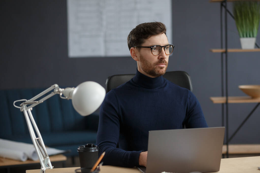Architekt pracující v kanceláři s laptopem. Obchodní portrét pohledného vousatého muže s brýlemi sedícími na pracovišti. Důvěryhodný obchodník uspěl. Obchodní koncept - Fotografie, Obrázek