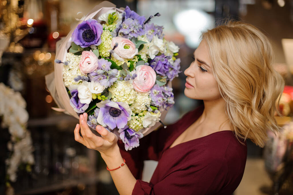 包装紙に紫、緑、バラ色の花の花束を持っている女性 - 写真・画像