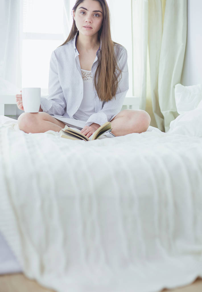 Woman sitting in bed reading a book and having breakfast - Photo, Image