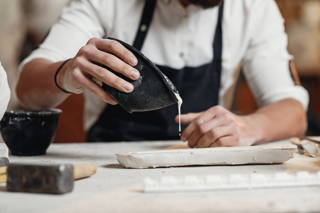 Der junge Bildhauer arbeitet in einer Gipserei. Handwerker gießt Gips in die Silikonform. - Foto, Bild