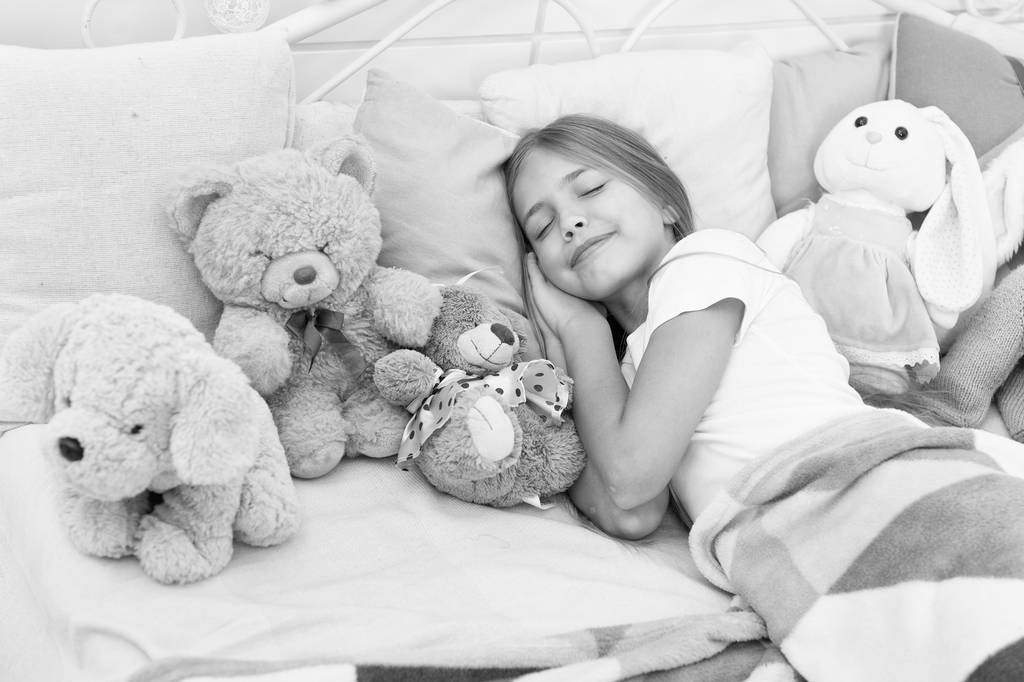 寝る前にリラックス。女の子はおもちゃで夜の時間をお楽しみください。子供は枕毛布の背景をおもちゃでベッドを置く。女の子の子供はパジャマを着る。寝る前に柔らかいおもちゃを再生します。おもちゃで寝なさい。子供時代の世話 - 写真・画像