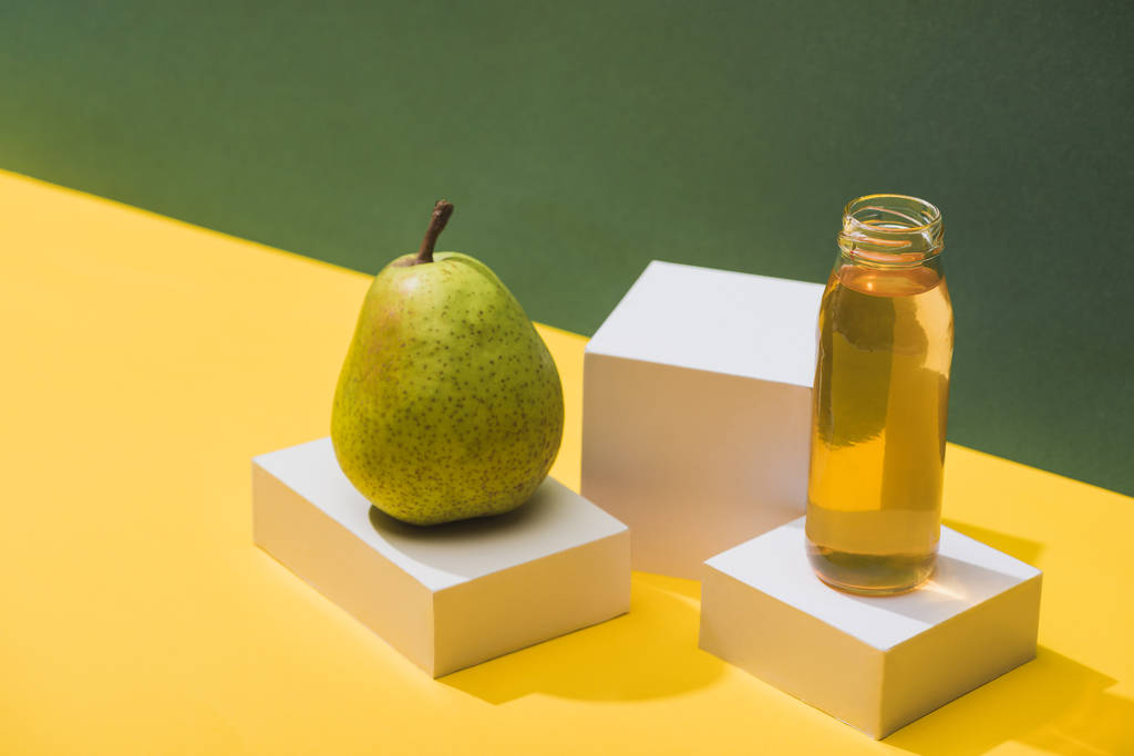 zumo fresco en botella cerca de pera y cubos blancos sobre fondo verde y amarillo
 - Foto, imagen