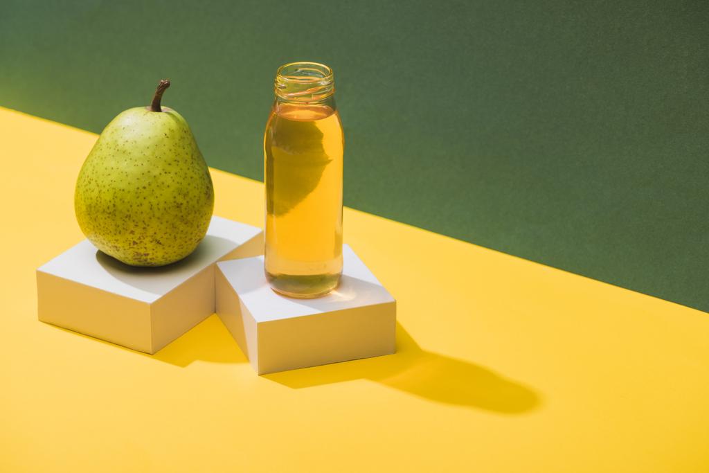 φρέσκος χυμός σε μπουκάλι κοντά σε αχλάδι και λευκούς κύβους σε πράσινο και κίτρινο φόντο - Φωτογραφία, εικόνα