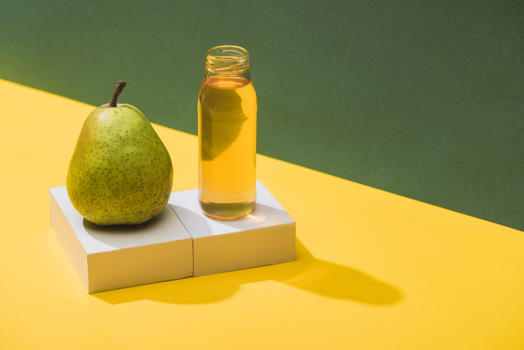 friss gyümölcslé palackban, körte és fehér kockák közelében, zöld és sárga alapon - Fotó, kép
