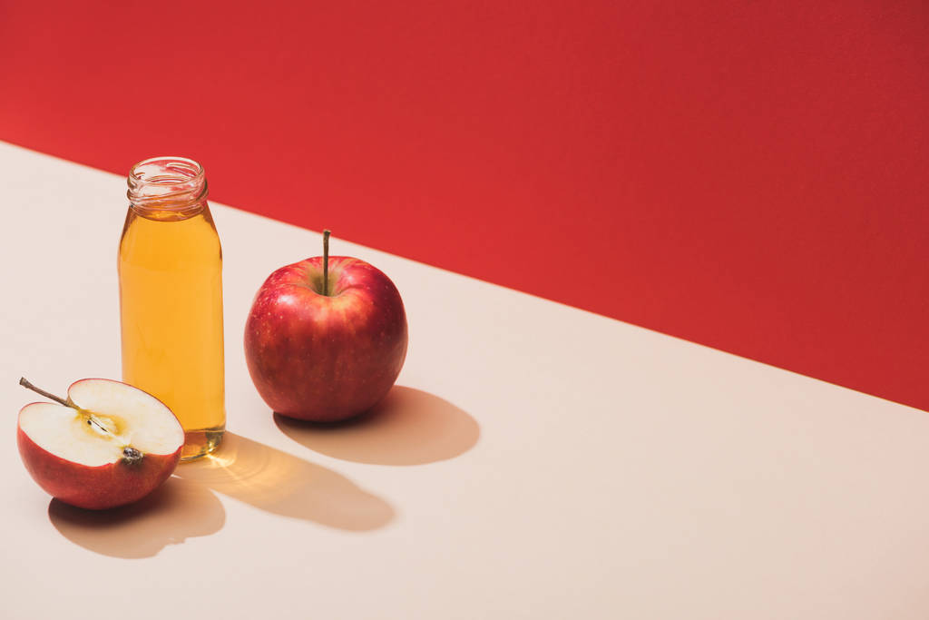 tuore mehu pullossa lähellä omenoita punaisella pohjalla
 - Valokuva, kuva