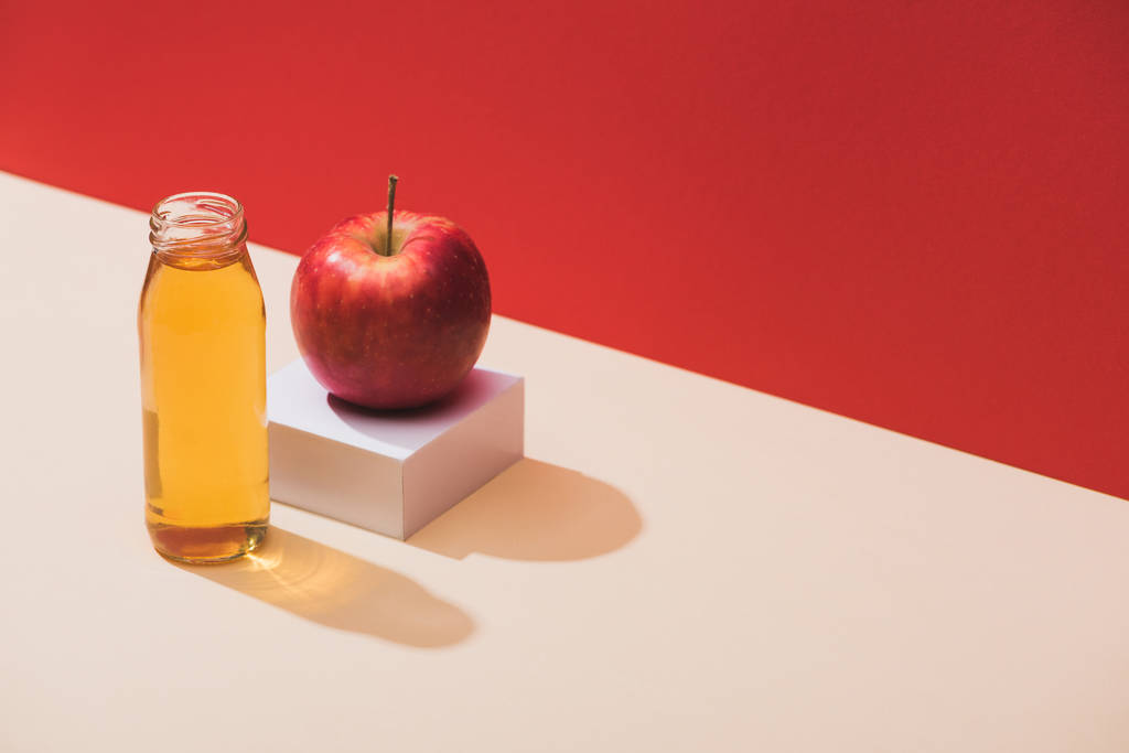 succo fresco in bottiglia vicino a mela e cubo bianco su sfondo rosso
 - Foto, immagini