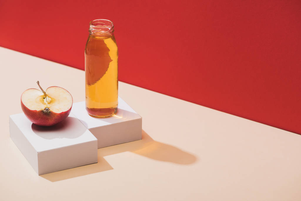 frischer Saft in der Flasche in der Nähe der Apfelhälfte und weiße Würfel auf rotem Hintergrund - Foto, Bild