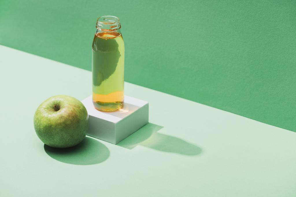 fresh juice near apple and and white cube on green and turquoise background - Fotoğraf, Görsel