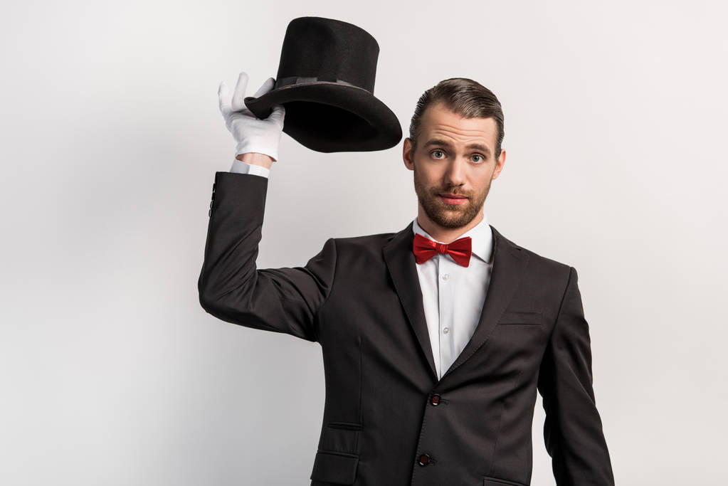 emotionele goochelaar in handschoenen met hoed, geïsoleerd op grijs - Foto, afbeelding