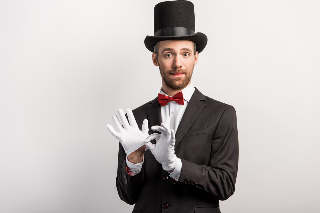 przystojny magik zdejmujący rękawiczki, odizolowany na szarości - Zdjęcie, obraz