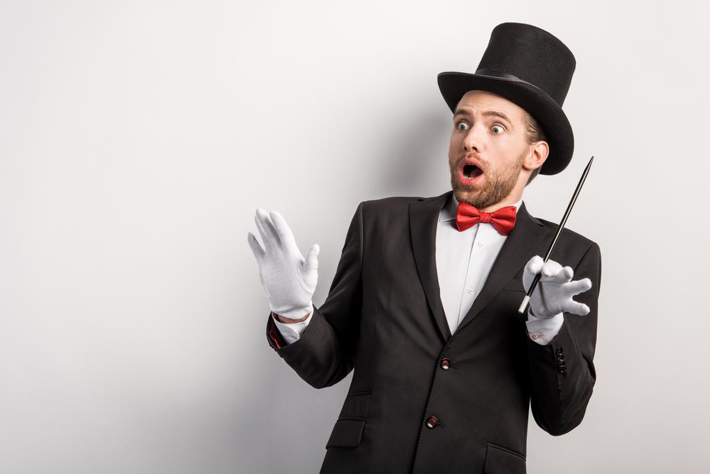 shocked magician with open mouth holding wand, isolated on grey - Photo, Image