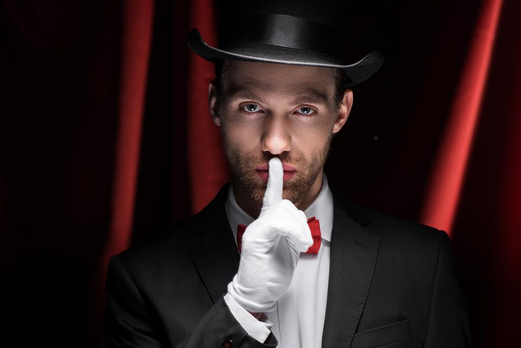 Zauberer zeigt Schweigesymbol im Zirkus mit roten Vorhängen - Foto, Bild