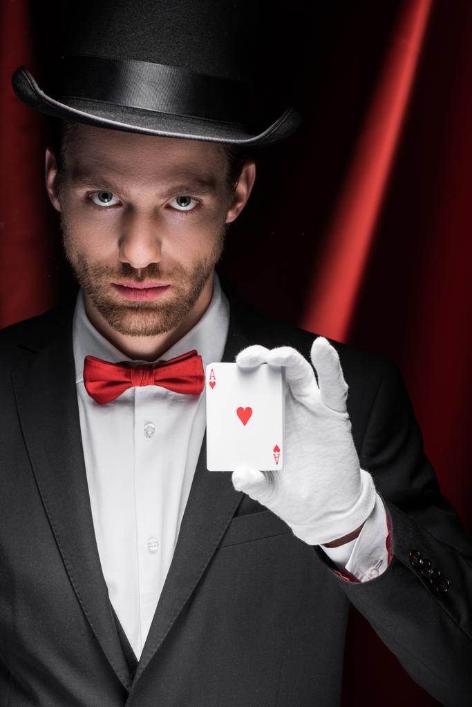 Profesyonel sihirbaz sirkte kırmızı perdeli oyun kartları tutuyor. - Fotoğraf, Görsel