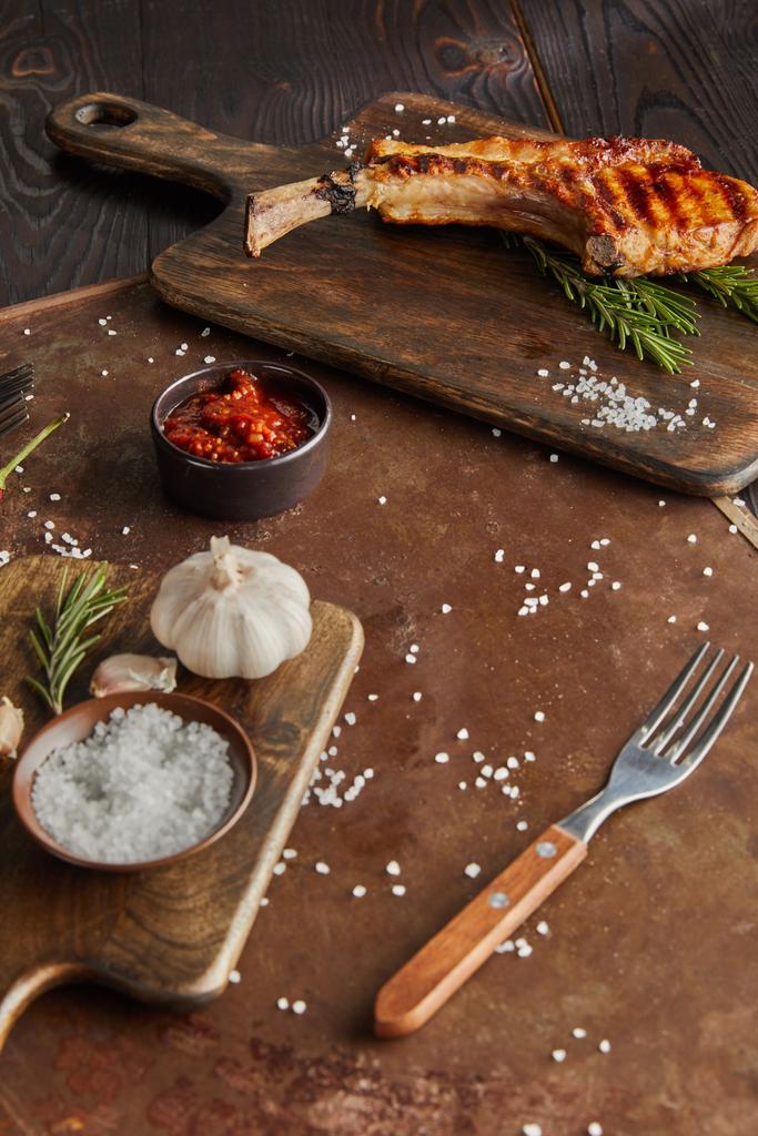 Focus selettivo di deliziosa bistecca ribeye sul tagliere con aglio e salsa di pomodoro su tavola di pietra su superficie di legno
 - Foto, immagini