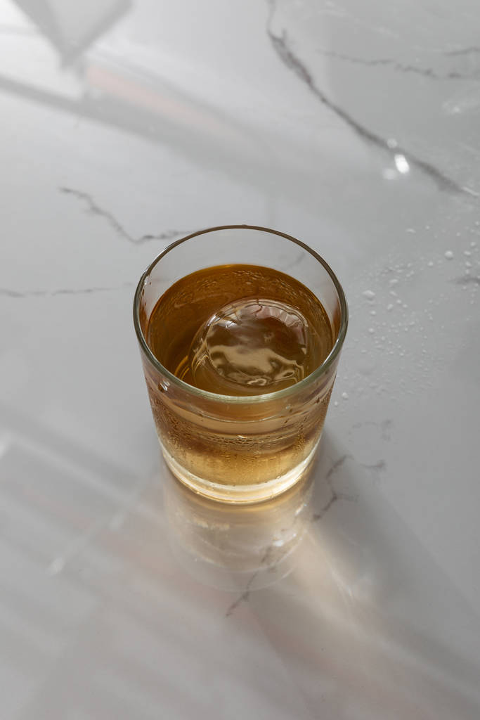 vrchní pohled na sklo s whisky a kostkou ledu na bílém mramorovém povrchu  - Fotografie, Obrázek