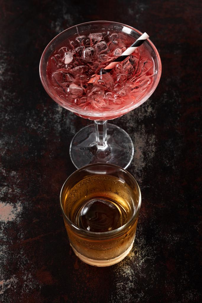 вид сверху на стекло с виски рядом с красным космополитическим коктейлем на черной поверхности
  - Фото, изображение
