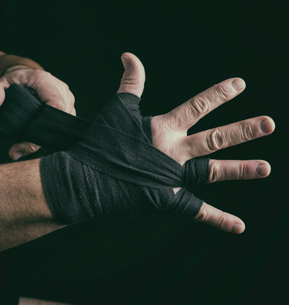 ο άνθρωπος τυλίγει τα χέρια του σε μαύρο ύφασμα επίδεσμο για σπορ, εσωτερικη - Φωτογραφία, εικόνα