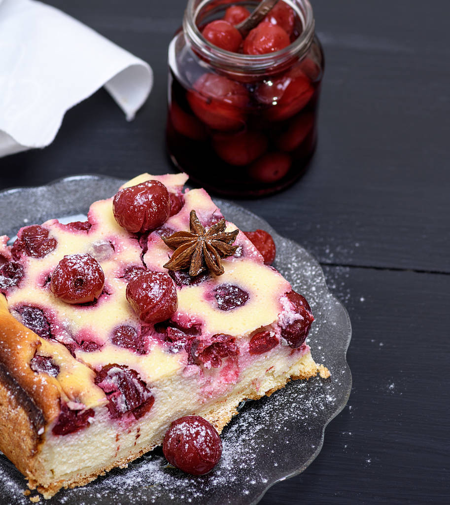 piece of a cheesecake with cherries on a glass plate and a jar with  berries - Photo, Image