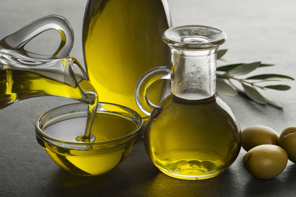 Olio di oliva biologico. Bottiglia di olio extra vergine versata nella ciotola di vetro - Foto, immagini