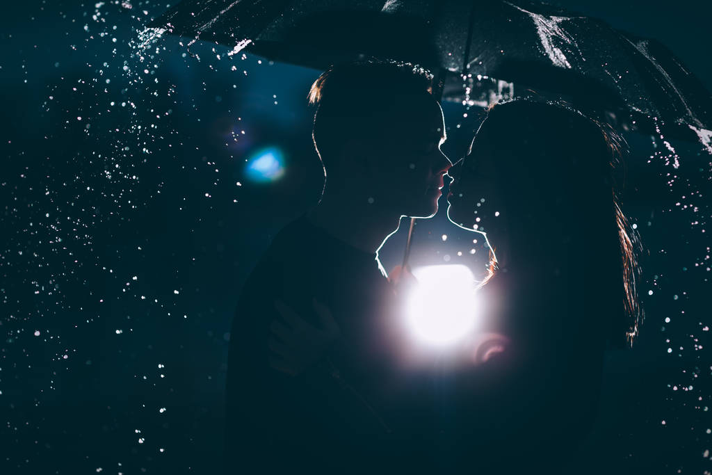 молодая пара, стоящая под тёмным зонтом
. - Фото, изображение