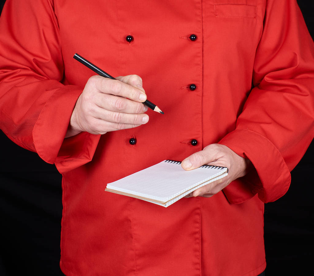 szakács piros egységes egy üres jegyzetfüzet és egy fekete fa ceruza, fekete háttér - Fotó, kép