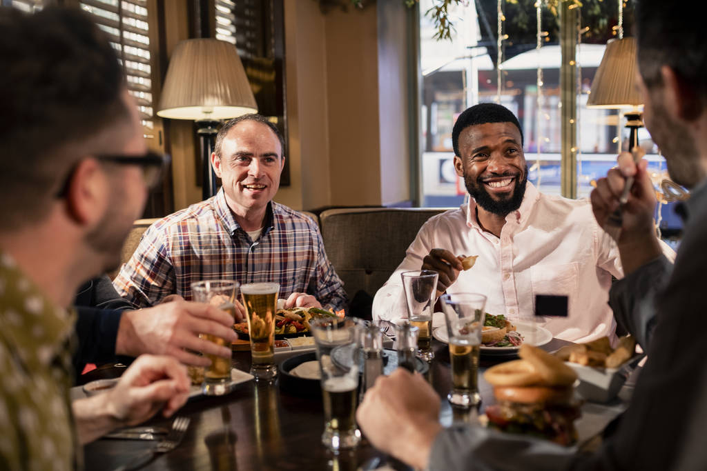Petit groupe d'amis masculins mi-adultes dégustant de la nourriture dans un restaurant. Ils parlent et apprécient l'autre compagnie. - Photo, image